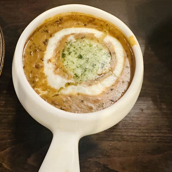 Creamy brown lentil dal with a swirl of white cream and green herb oil in a white bowl.