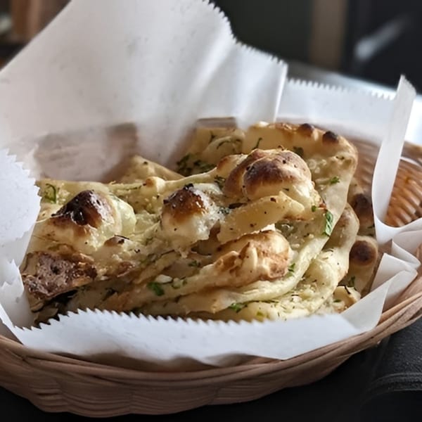 A basket of freshly baked naan bread, garnished with herbs and spices, lined with white paper.