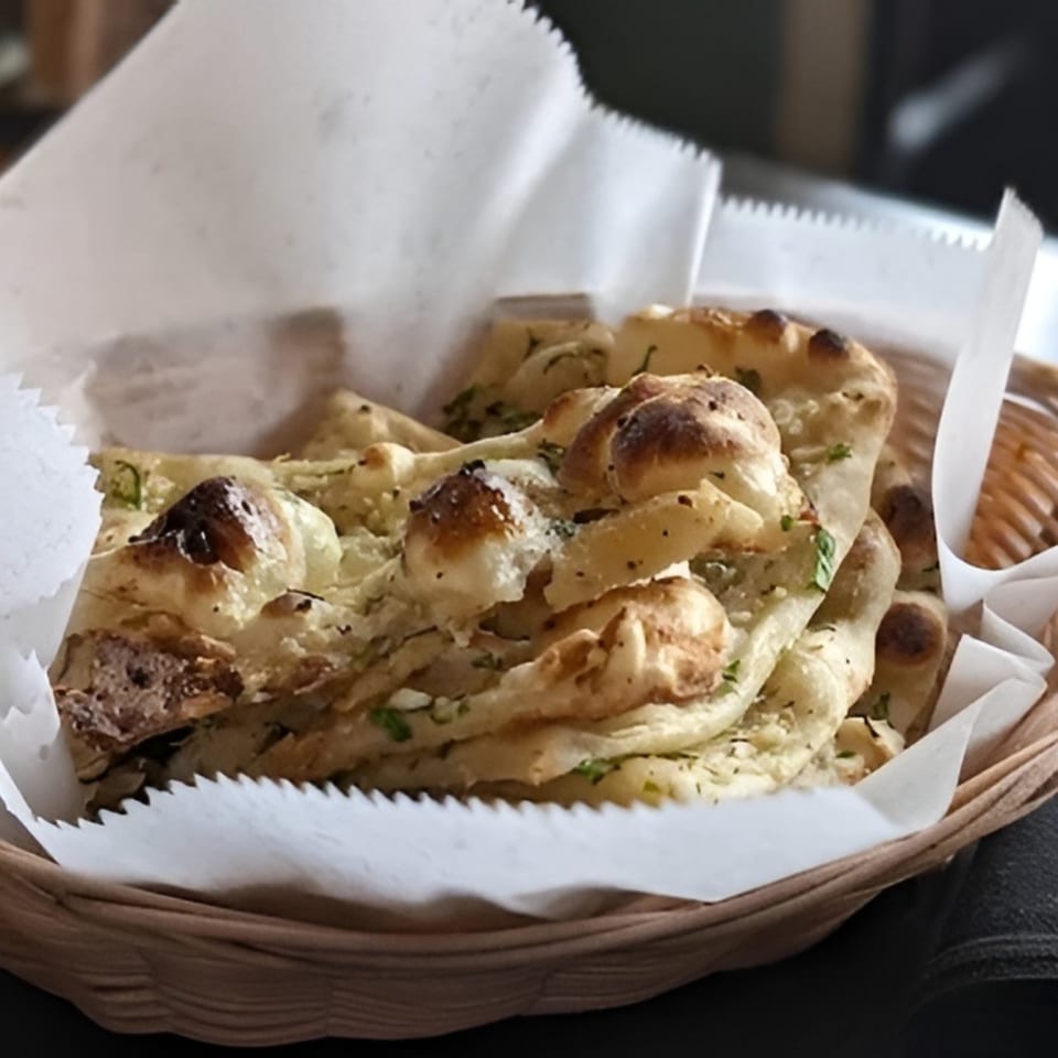 A basket of freshly baked naan bread, garnished with herbs and spices, lined with white paper.