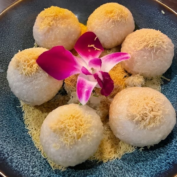 Six round mochi-like desserts with yellow shredded topping, garnished with a pink orchid on a blue plate.