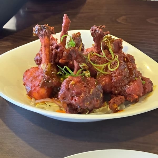 A white plate filled with red, saucy chicken lollipops garnished with green herbs.