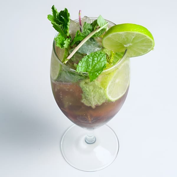 A refreshing mojito cocktail in a wine glass, garnished with fresh mint, lime slices, and ice.