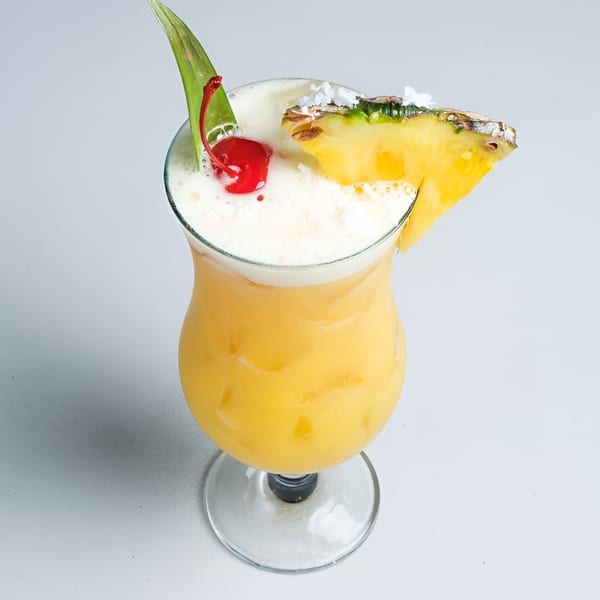 Tropical yellow cocktail with a foamy top, garnished with a pineapple slice, cherry, and green leaf.