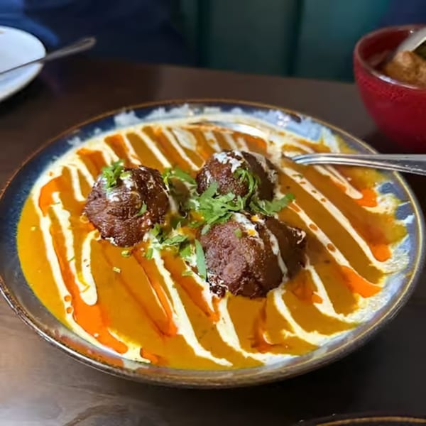 Three dark brown meatballs with green herbs sit in a yellow and orange sauce with white swirls.