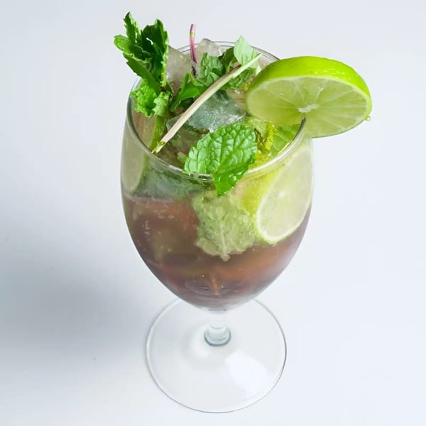 A refreshing Artha Indian Bistro cocktail with mint, lime, and ice in a stemmed glass.