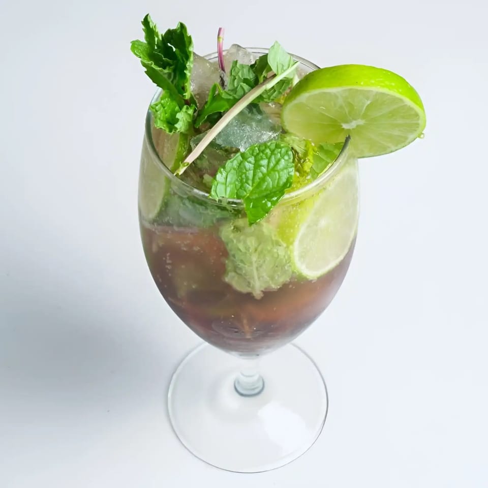 A refreshing Artha Indian Bistro cocktail with mint, lime, and ice in a stemmed glass.